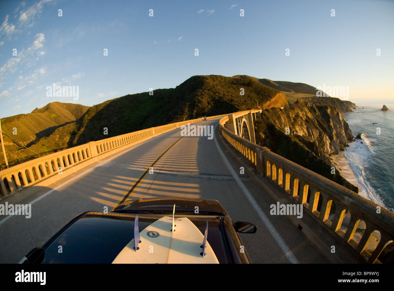 Un coche con una tabla de surf en la parte superior de viajar durante los Bixby Creek Bridge, en la autopista 1 en Big Sur, California, Estados Unidos. Foto de stock