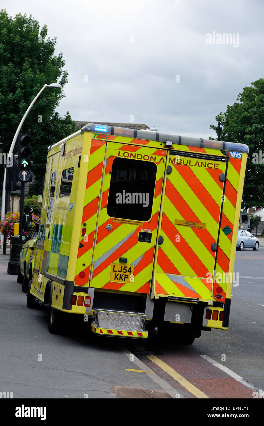 Londres ambulancia estacionada la mitad sobre pavimento con luces parpadeantes mientras asistíamos una emergencia Foto de stock