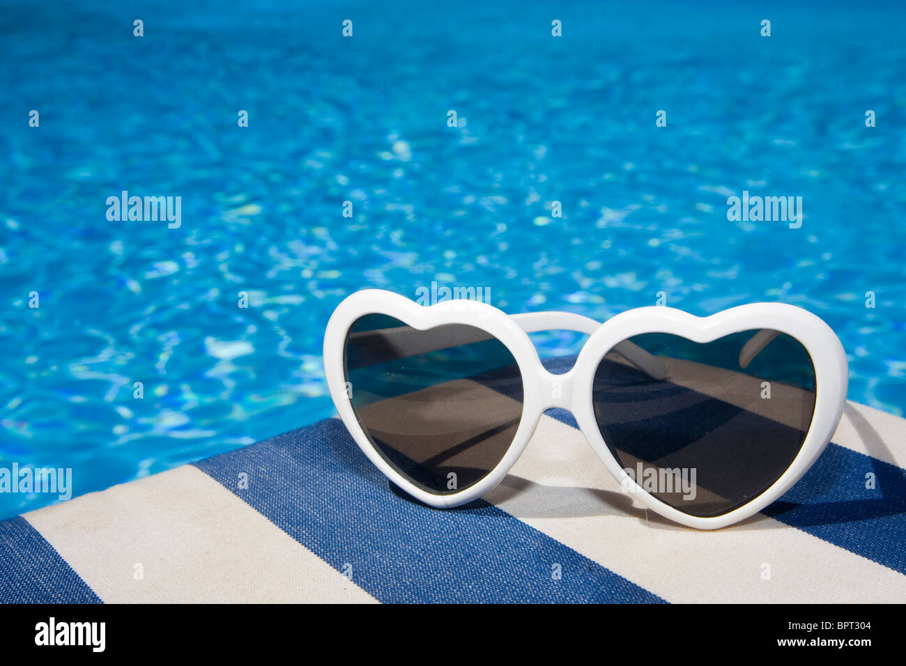Gafas de sol en forma de corazón por una piscina de color azul Foto de stock