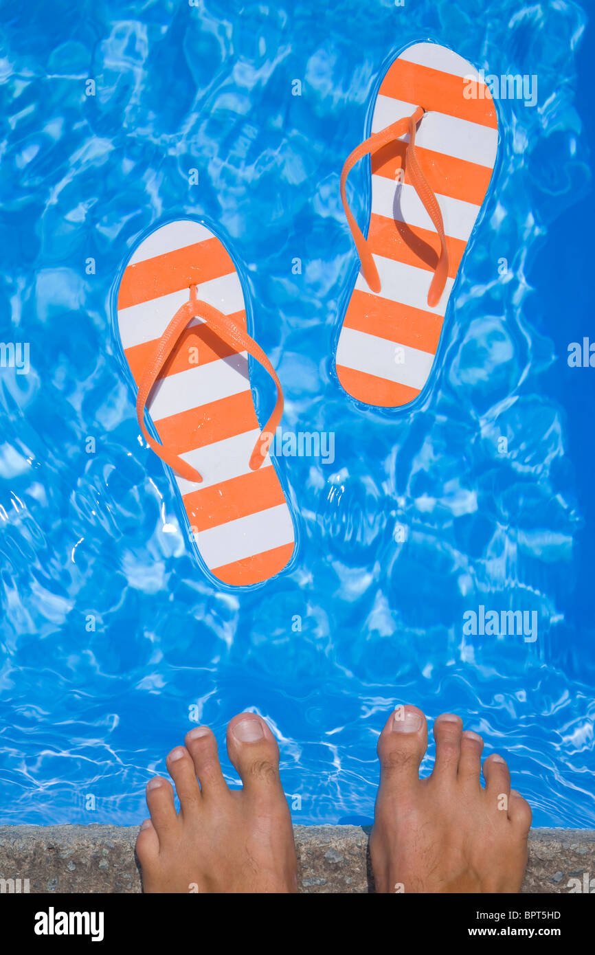 Stripey bastante par de sandalias o chanclas en un reluciente piscina de  color azul con los pies del hombre Fotografía de stock - Alamy