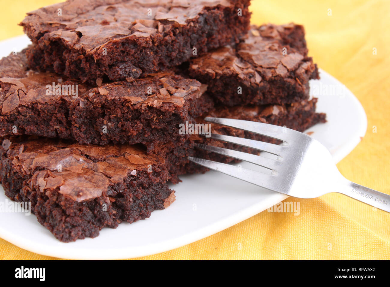 Chocolate Fudge brownies en un plato con un tenedor sobre un mantel amarillo Foto de stock