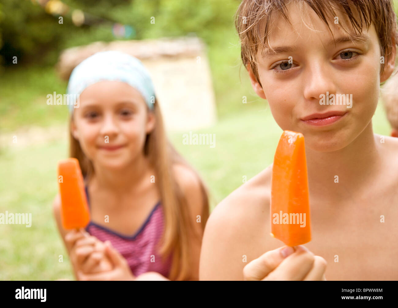 Muchacho y muchacha comiendo helado de naranja lolly Foto de stock