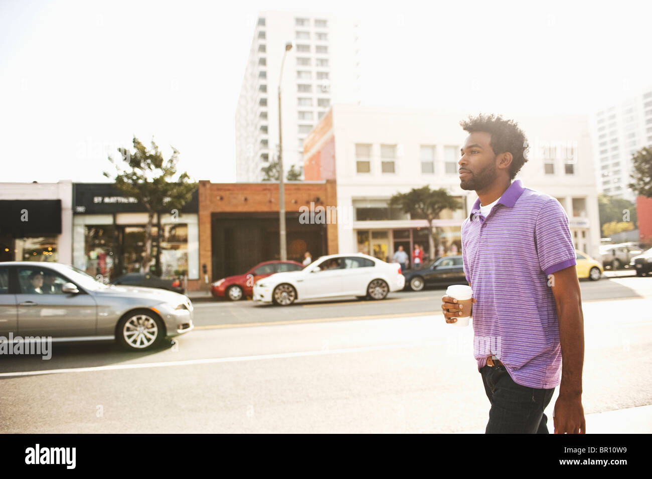Hombre afroamericano con la taza de café de caminar sobre la acera Foto de stock