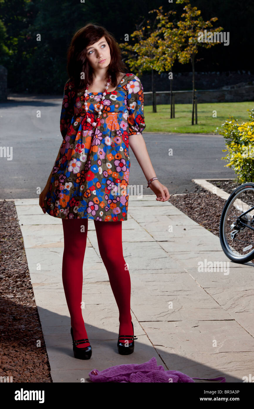 Una mujer joven con cabello oscuro y rojo brillante vistiendo leotardos adopta una pose de moda. Foto de stock