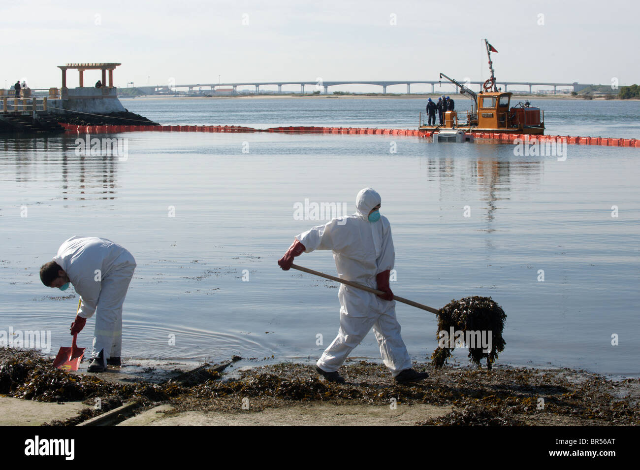 Los hombres en el cuerpo completo de ropa protectora y máscaras respiratorias limpie la base mientras un barco sella la bahía con boyas Foto de stock