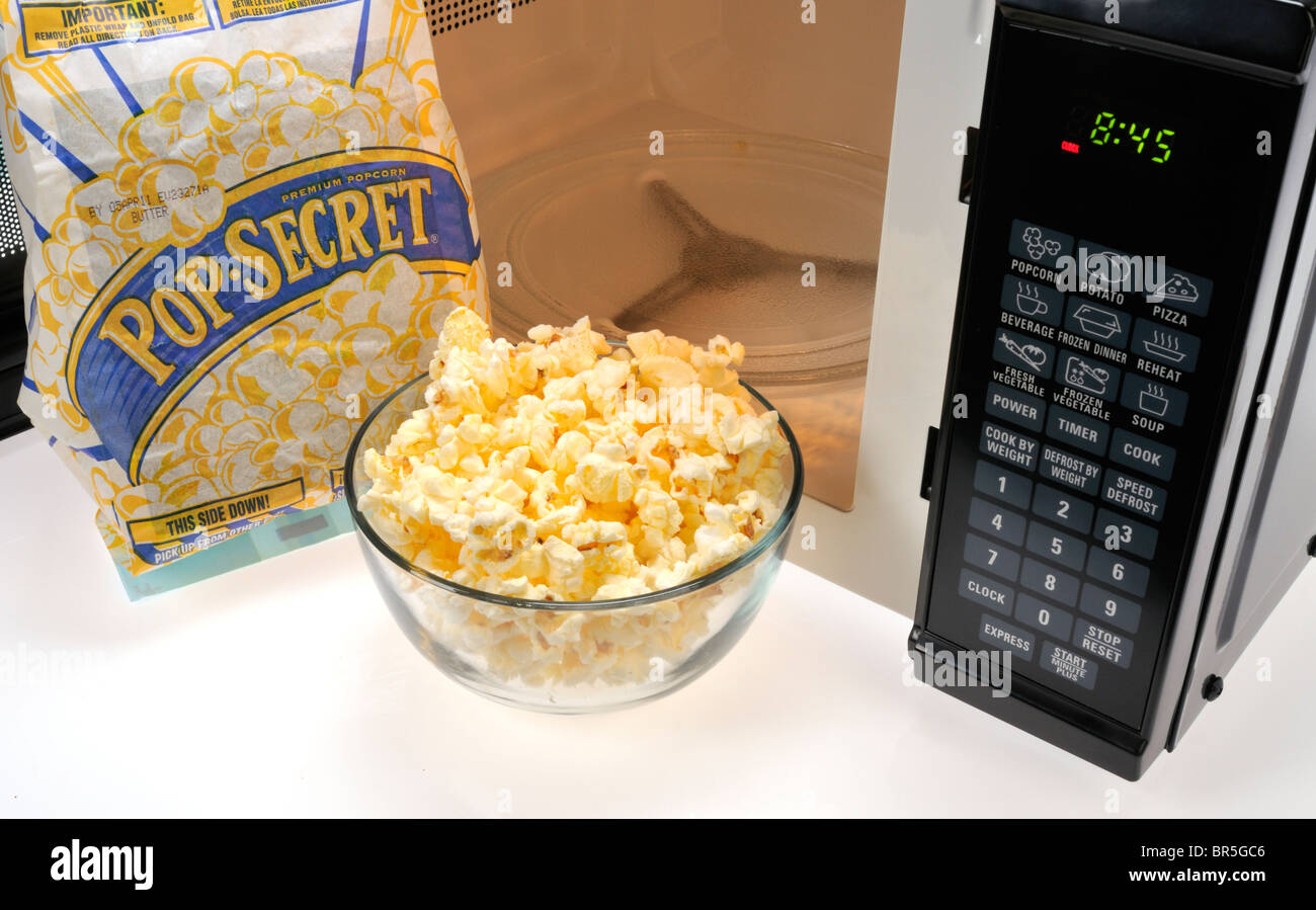 Abra la bolsa de Pop Secret con un tazón de vidrio de palomitas de maíz cocido y delante del horno. Studio. Foto de stock