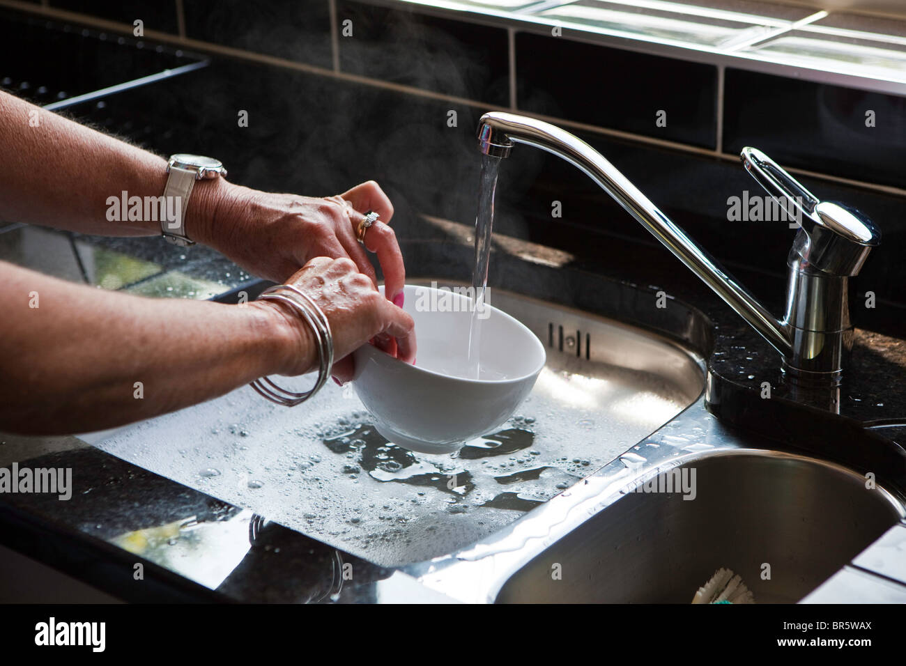 Una mujer lava los platos con agua caliente suministrada por un Willis Energías Renovables Solar sistema de sifón. Foto de stock