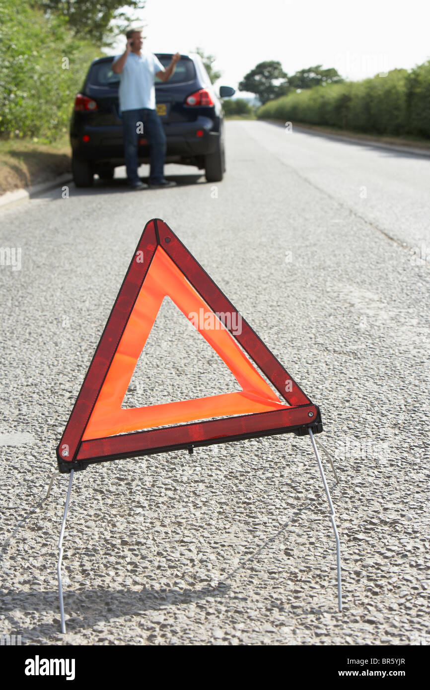 Conductor, desglosado por país por carretera con señal de advertencia en primer plano Foto de stock