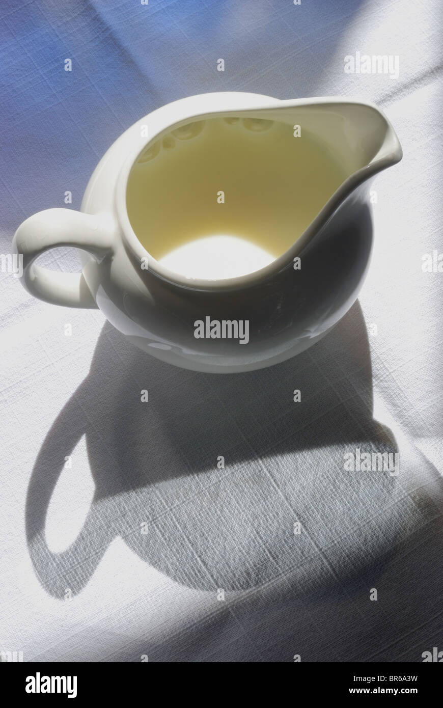 Cerámica Blanca Pequeña / cerámica, jarra de leche/crema jarra sobre una textura de fondo de lino. Gráfico con profundas sombras. Foto de stock