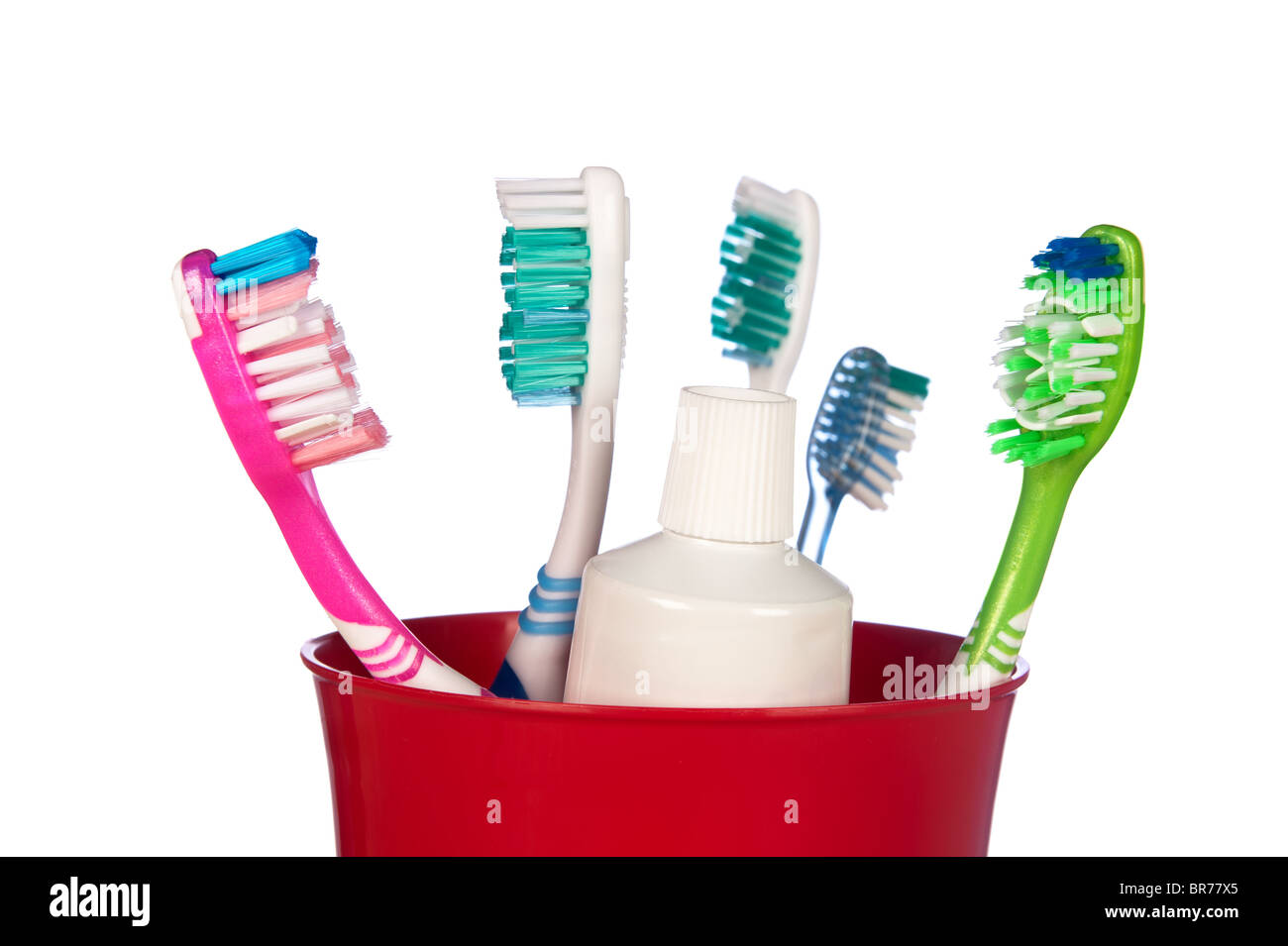 Los cepillos de dientes y un tubo de pasta de dientes en un recipiente aislado en blanco. Foto de stock