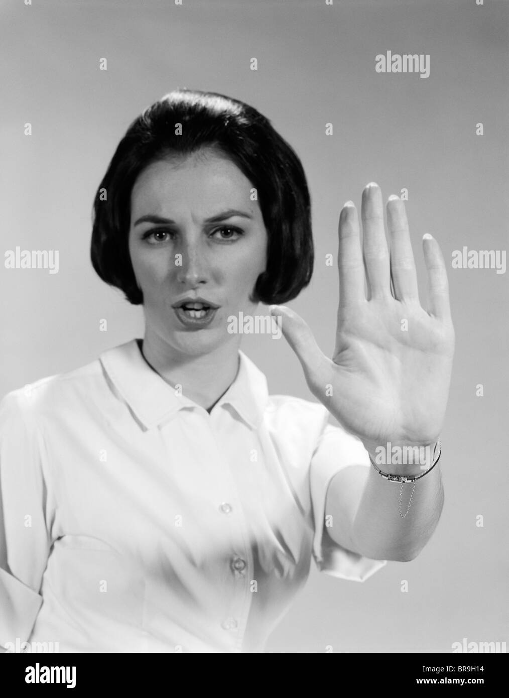 1960 MUJER mirando a la cámara sosteniendo la palma de la mano hacia adelante ordenando DETENER Foto de stock