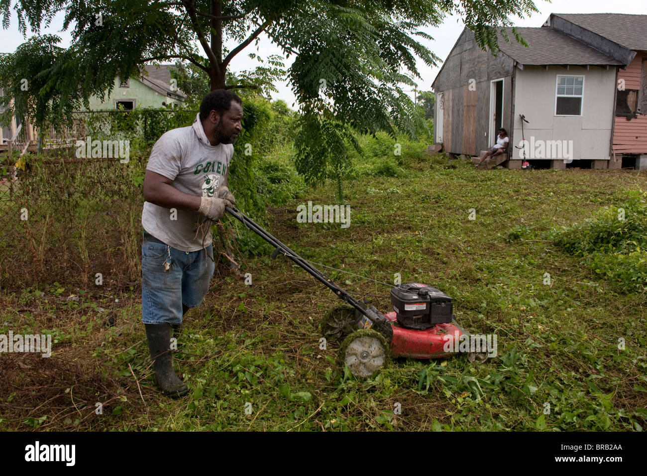 Un hombre corta la maleza desde el patio de su casa reconstruida parcialmente en Nueva Orleáns, Louisiana's Ninth Ward. Foto de stock