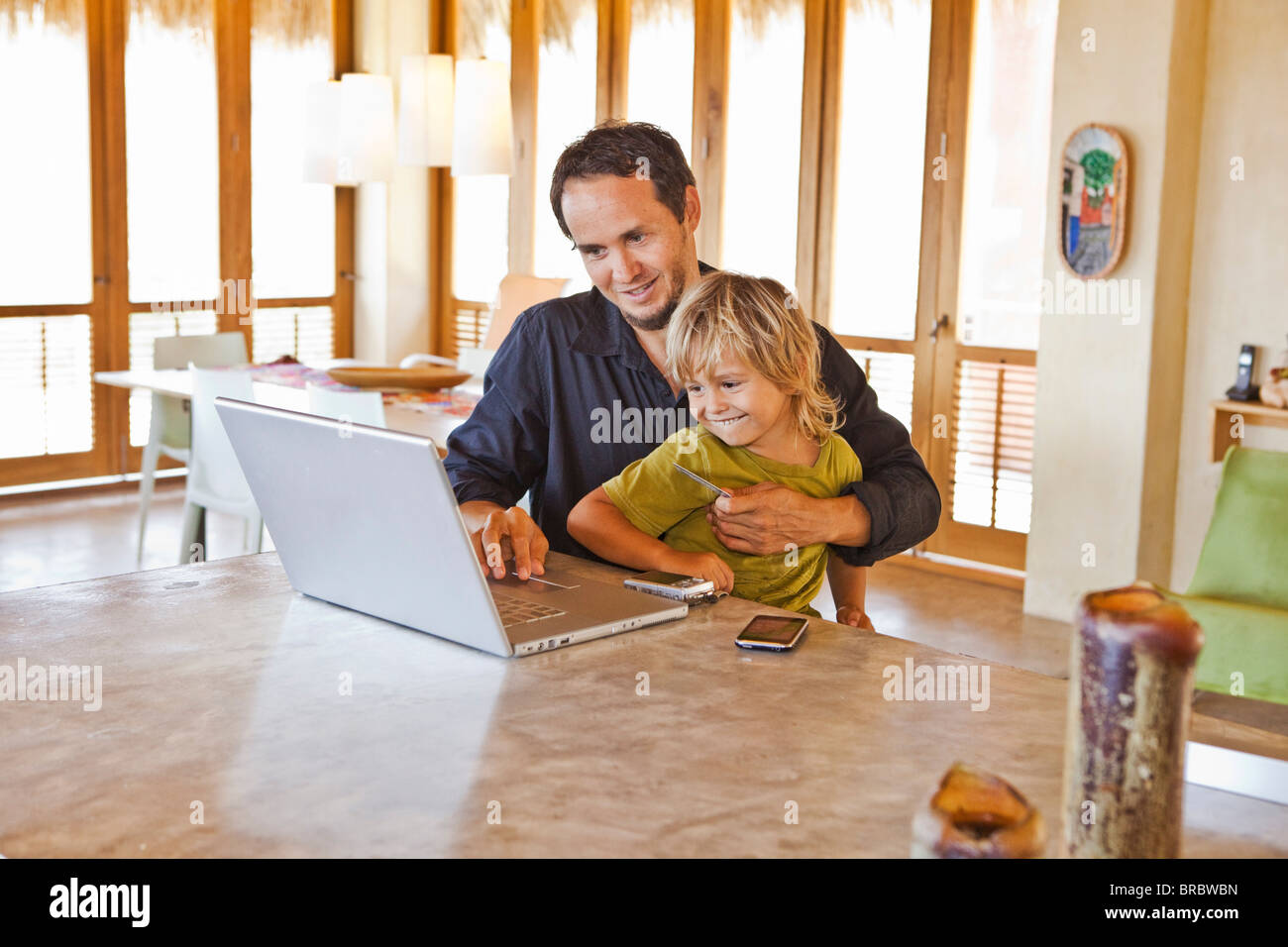 Hombre trabajando con un portátil con el niño en la vuelta Foto de stock