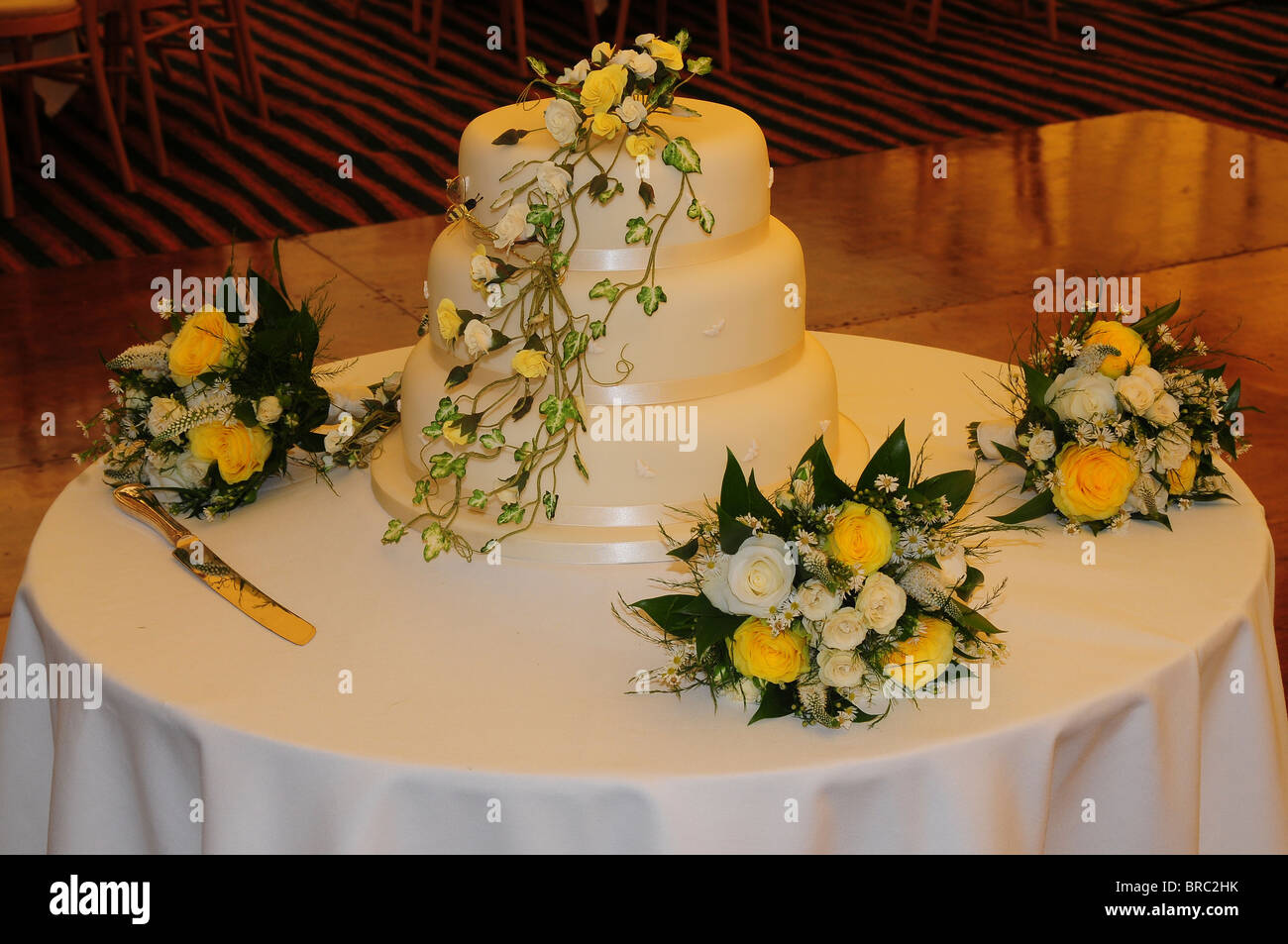 El tradicional pastel de bodas blanco de tres niveles en la mesa de recepción con ramos de rosas amarillas y blancas. Dorset, UK 2009 Foto de stock