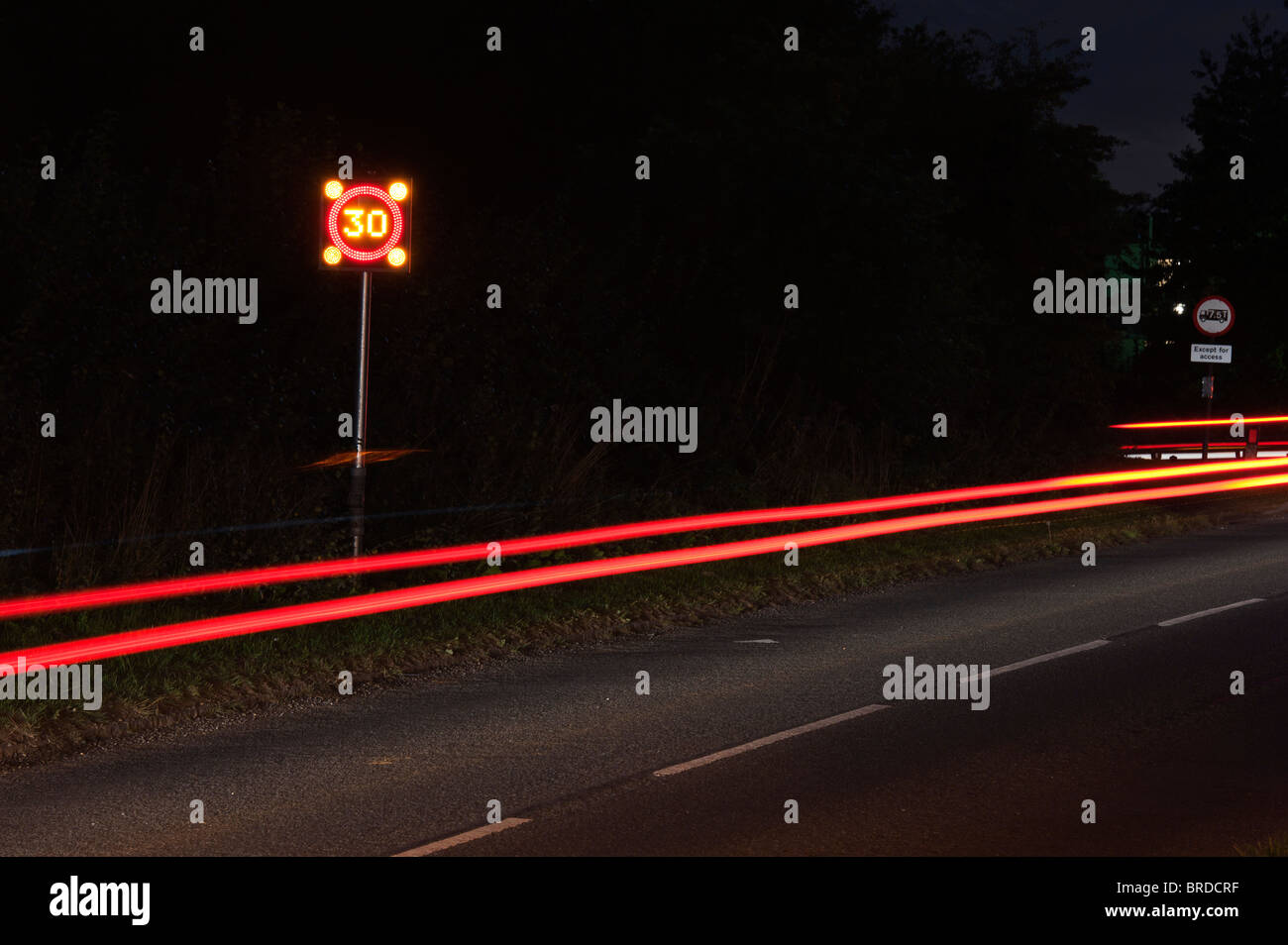 Parpadear 30mph velocidad firmar en una aldea y luces de cola de coches durante la noche. La larga exposición Foto de stock