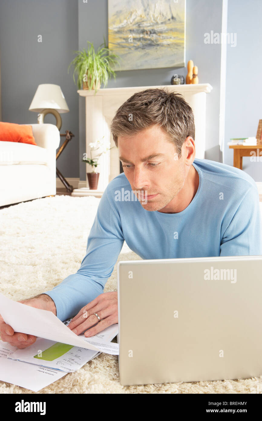 Hombre utilizando el portátil para gestionar los recibos del hogar sentar sobre una alfombra en casa Foto de stock