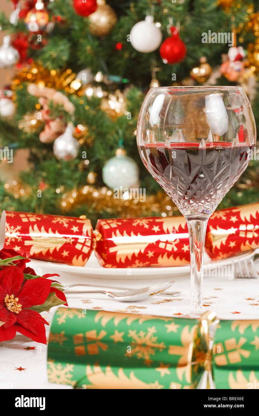 Chistmas crackers, árbol de navidad y un cristal con vino en una mesa de comedor Foto de stock