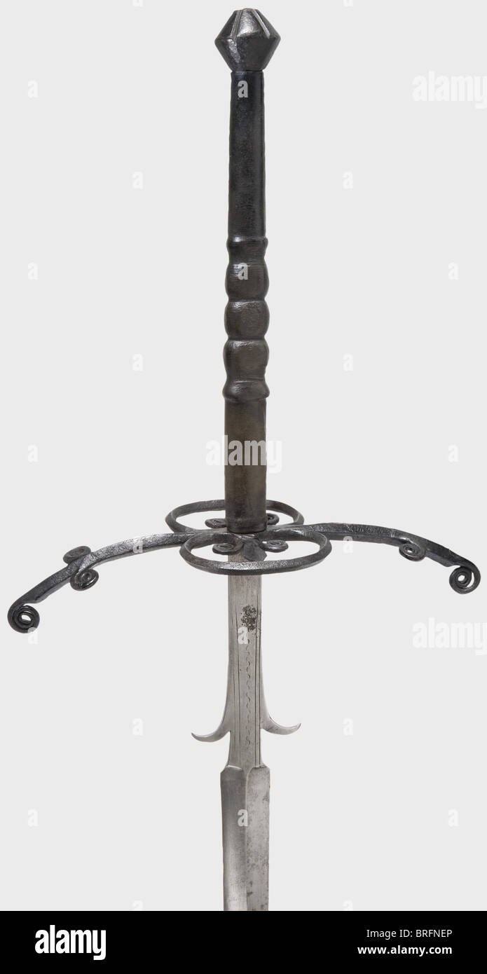 Una espada alemana de dos manos, alrededor de 1580. Hoja masiva, con  reborde en ambos lados. Los ricasos largos tienen ganchos de unión curvos y  líneas decorativas estampadas. Quillons ennegrecidos con finales