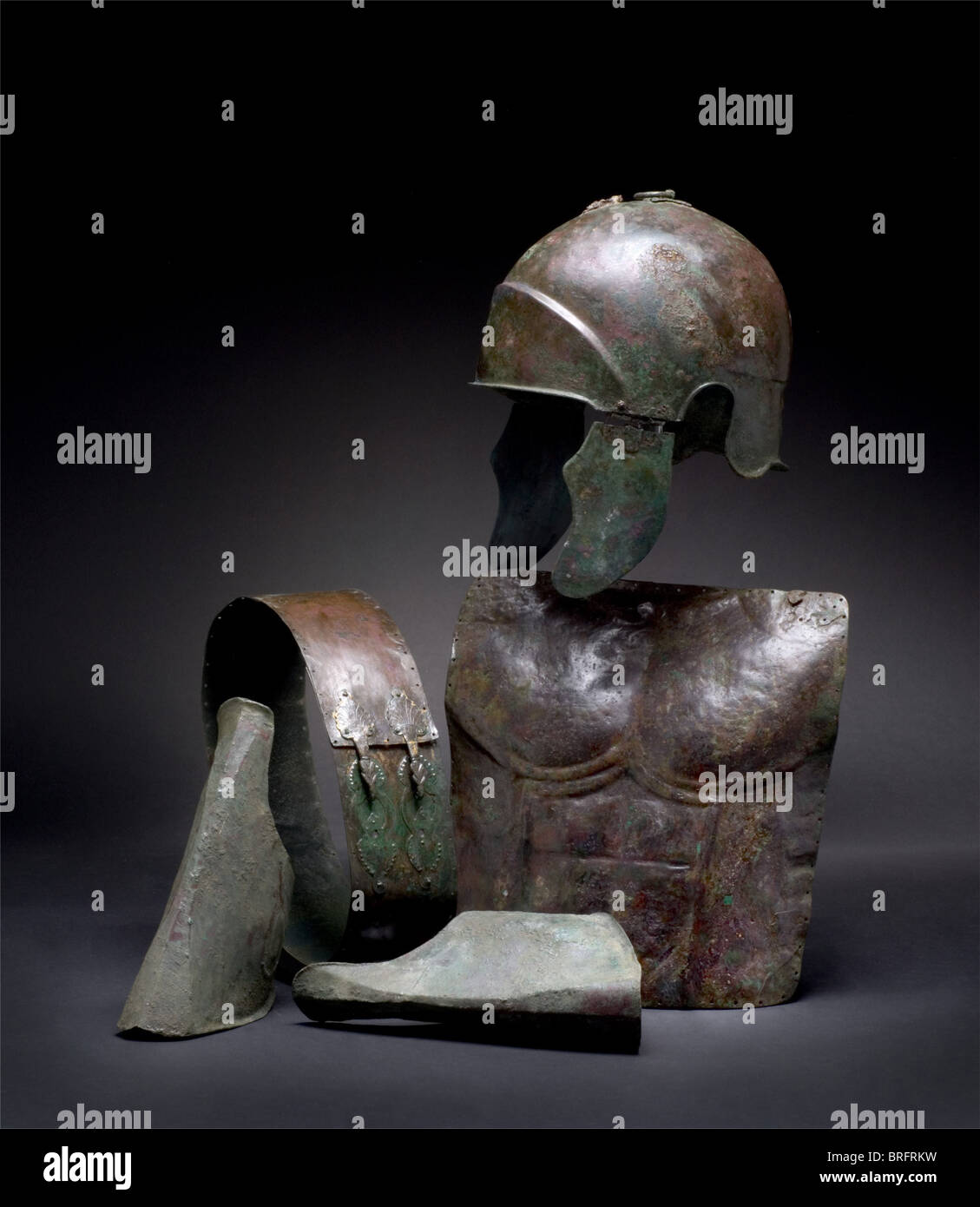 Un conjunto de armadura cursiva, siglo V/4 B.C.que consta de: Un casco de  bronce de Calcidian. La frente tiene un frontón grande en forma de arco, y  cortes de oído en los