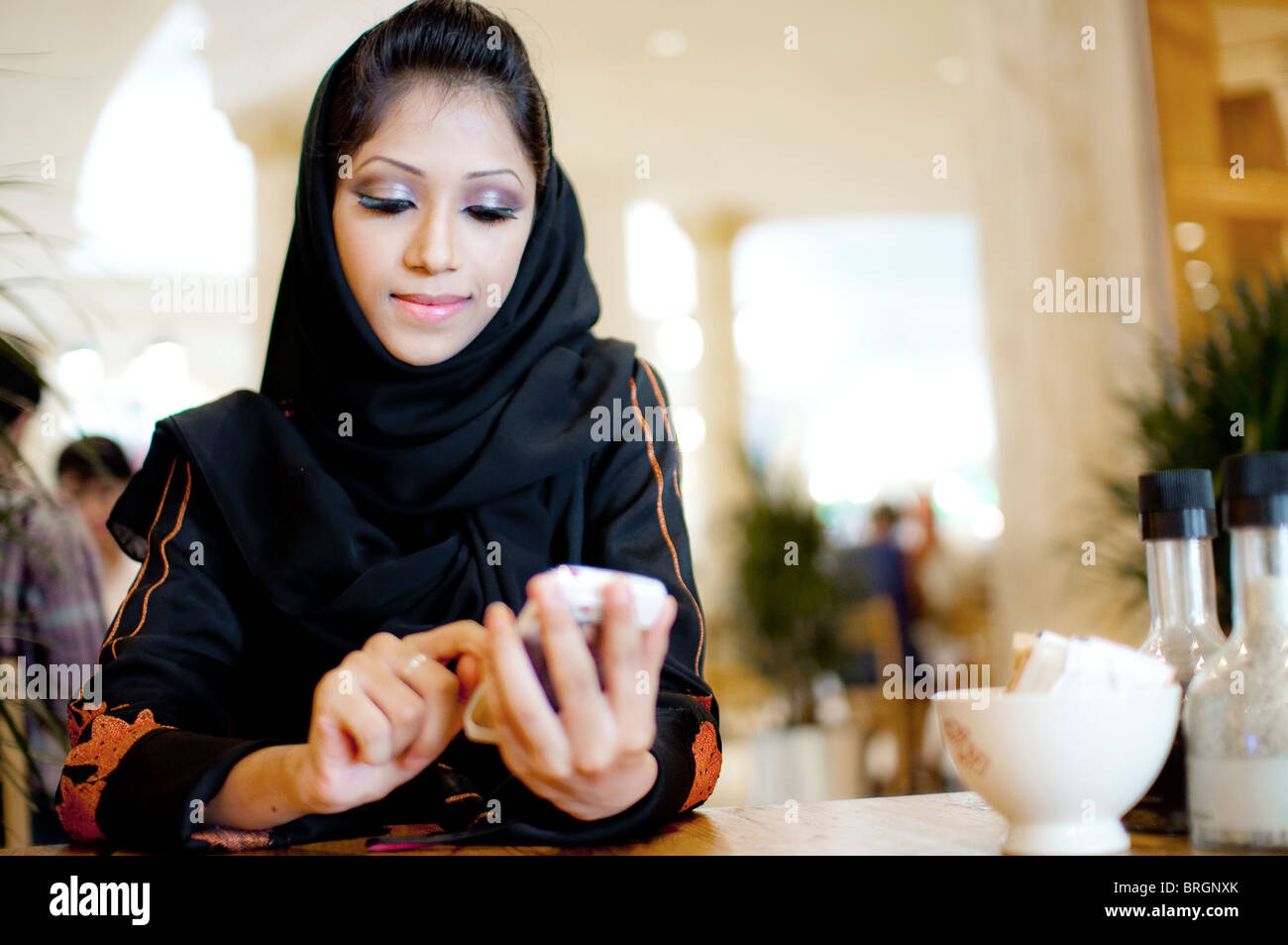 La joven moderna y rica liberó a la mujer árabe usando un burka aplicación móvil o mensajes de texto o registro en café brillante tienda Foto de stock