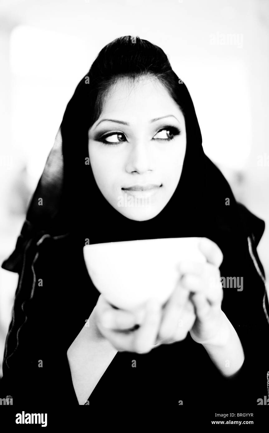 Hermosas mujeres árabes sentadas en una cafetería bebiendo café mientras observan, piensan y disfrutan de su entorno Foto de stock