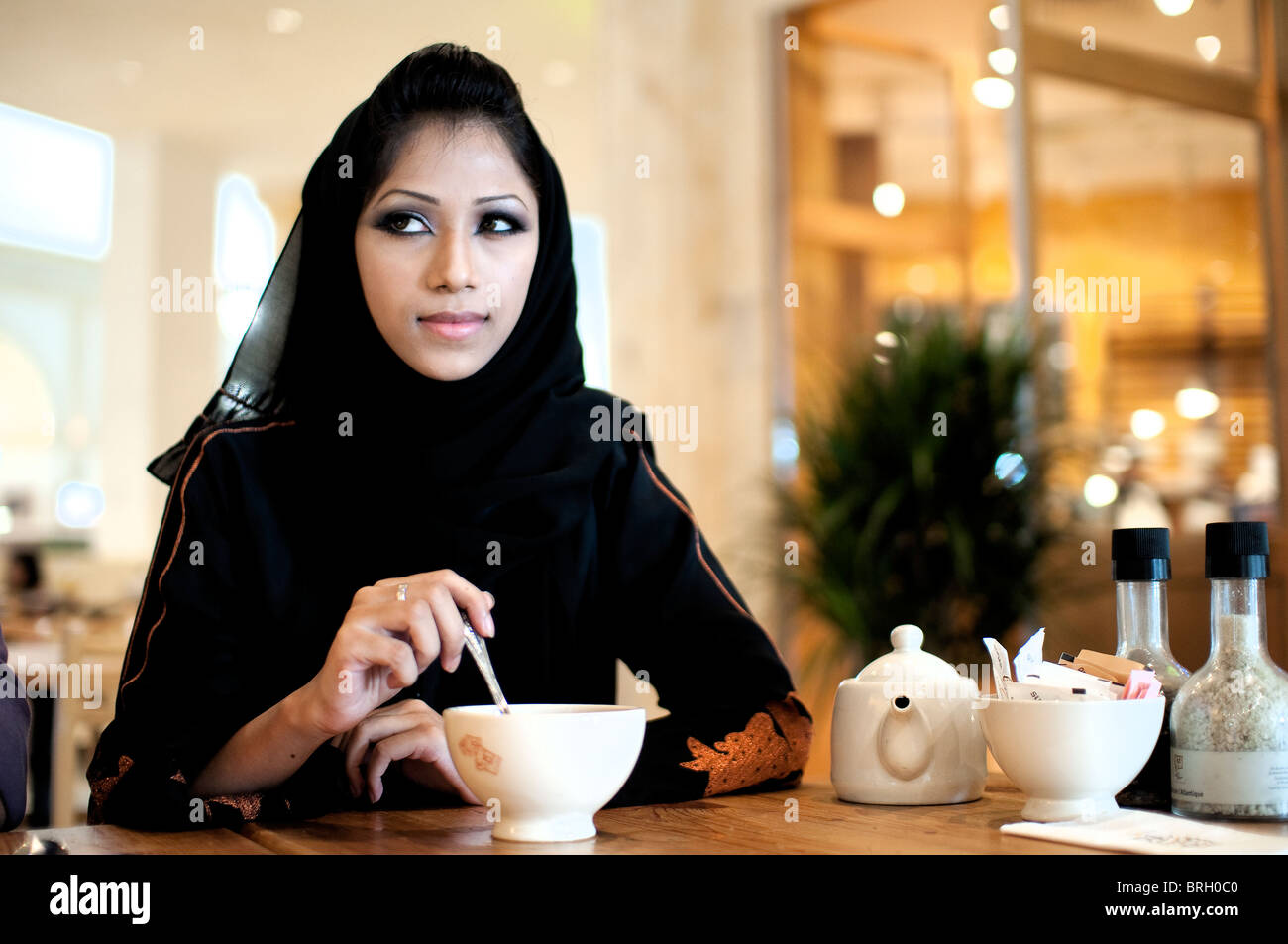 Hermosas mujeres árabes sentadas en una cafetería bebiendo café mientras observan, piensan y disfrutan de su entorno Foto de stock