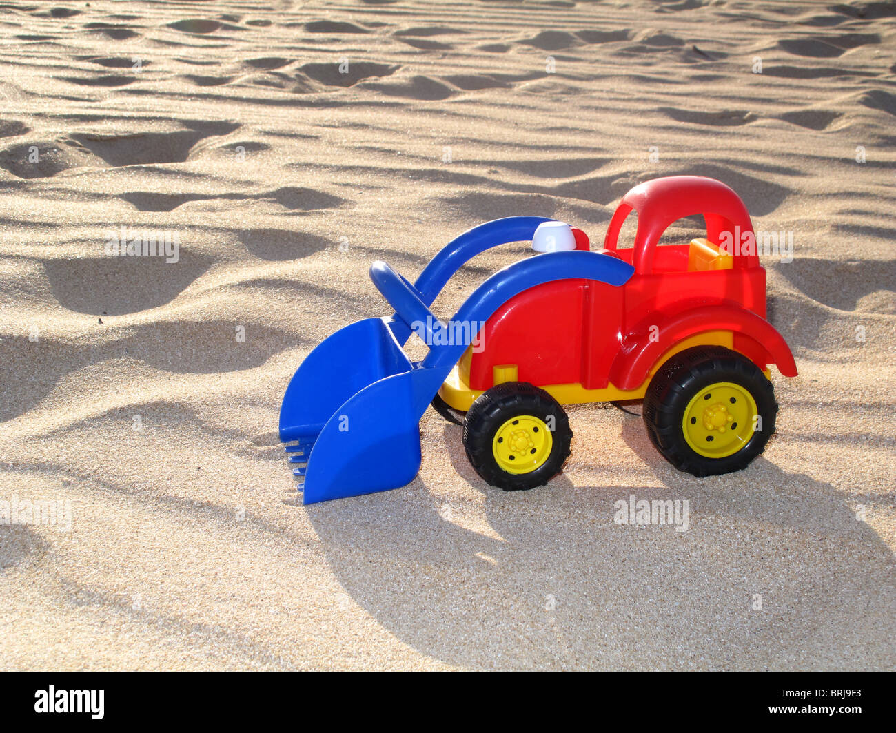 Camión de juguete de plástico de colores brillantes en la playa de arena Foto de stock