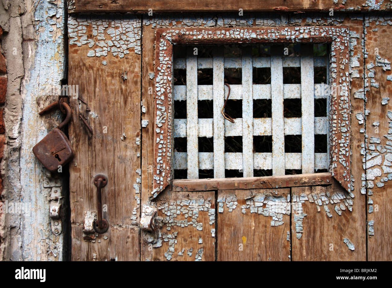 Antigua puerta de madera desgastada con barras en la ventana Foto de stock