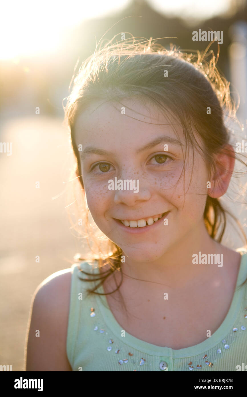 Una niña con pecas está sonriendo a la cámara con el sol brillando en el fondo. Foto de stock