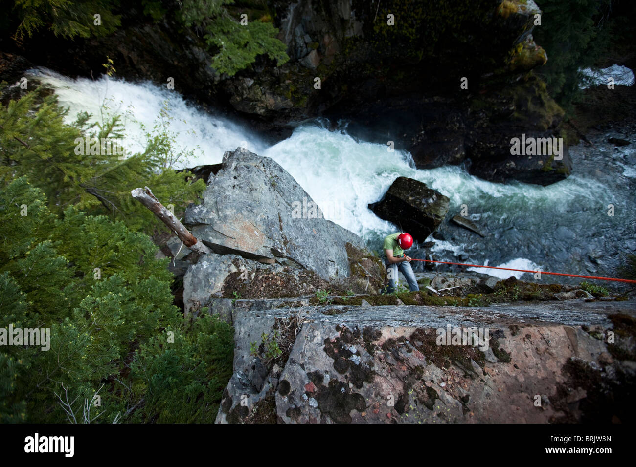 Un hombre joven rappel por un acantilado junto a una cascada en Idaho. Foto de stock