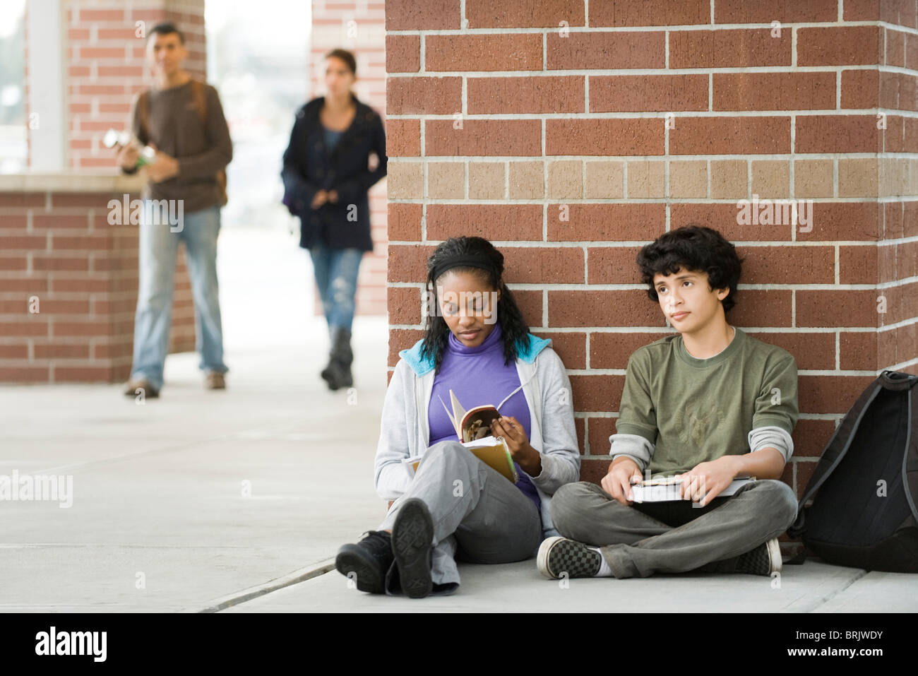 Los estudiantes sentados juntos en la acera de la escuela Foto de stock
