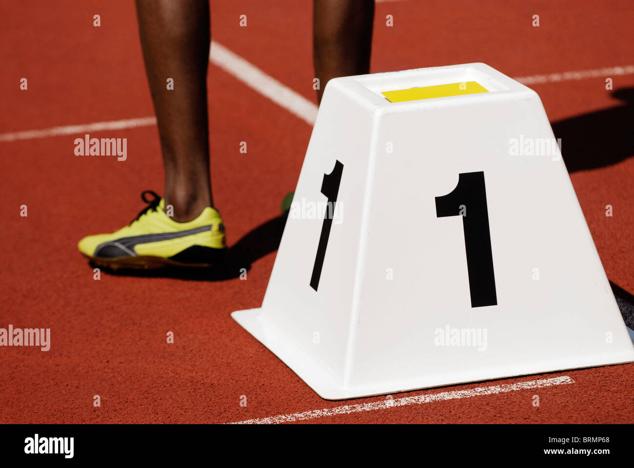Las piernas de un velocista masculino junto al bloque de partida número uno de la pista de atletismo fuera Foto de stock