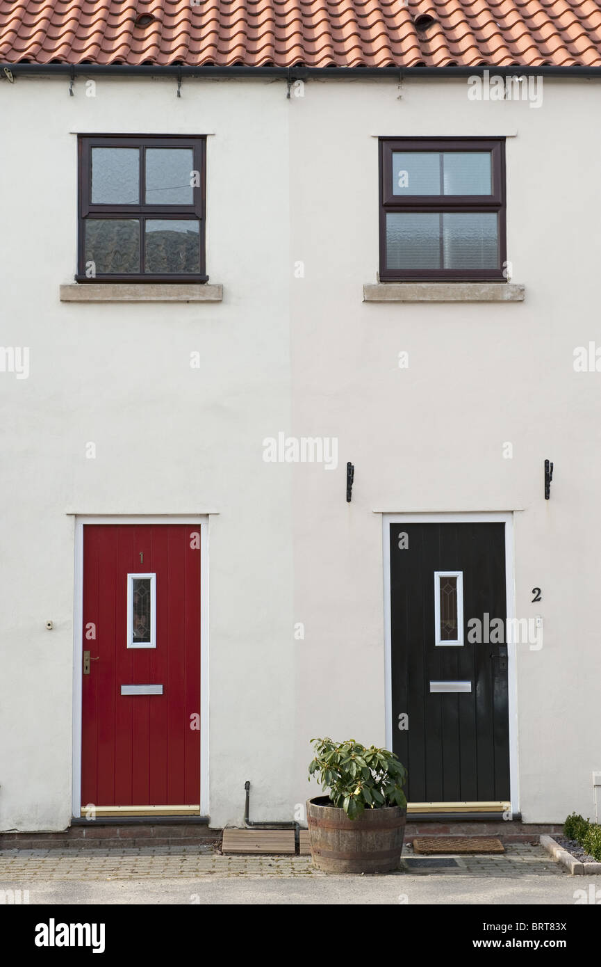 Dos puertas, uno rojo, uno negro y dos ventanas de arriba al lado de la otra en la parte delantera de una casa adosada. Foto de stock
