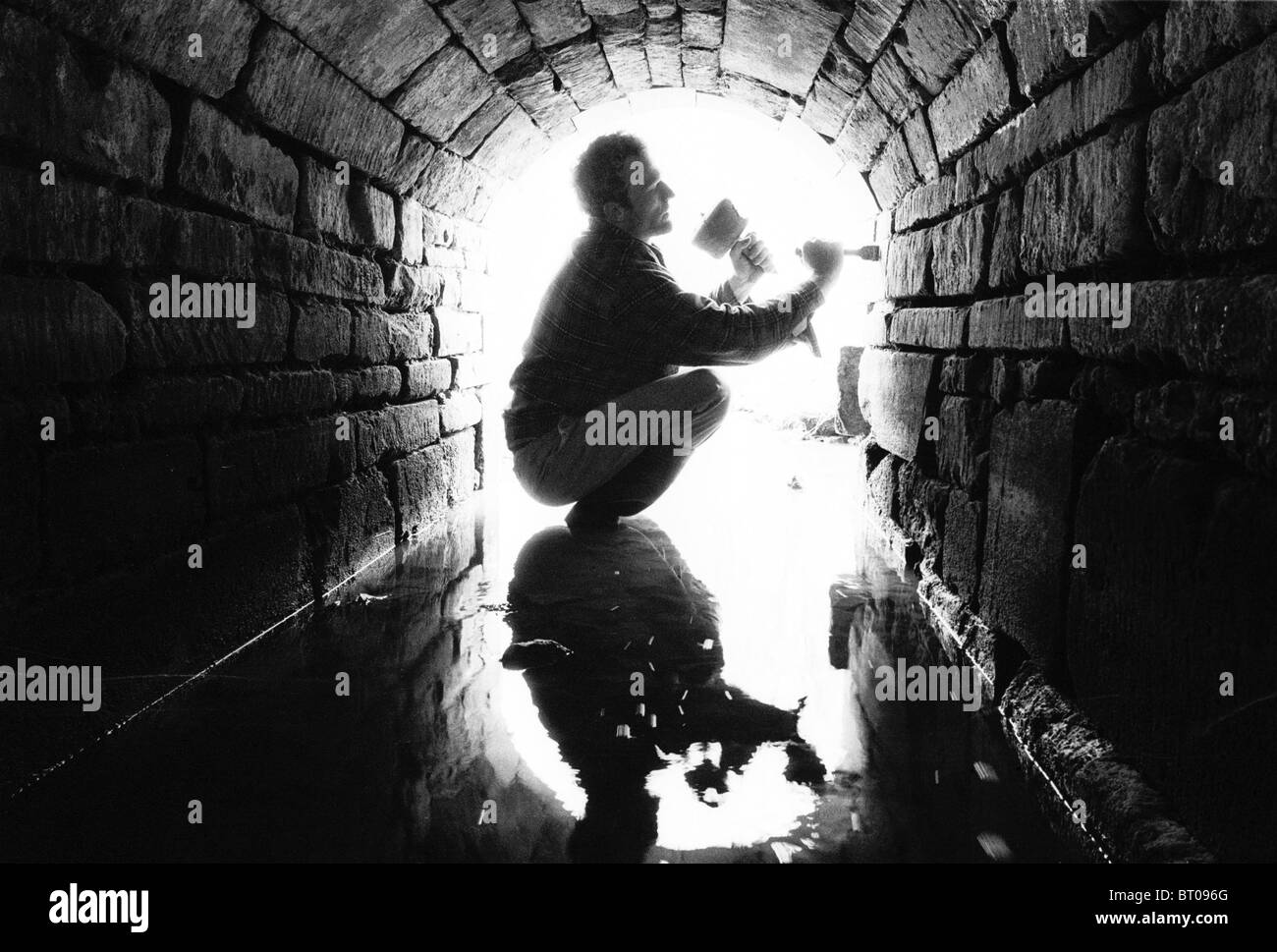 Un albañil en el trabajo en un canal de drenaje de piedra en los terrenos de una casa señorial. Foto de stock