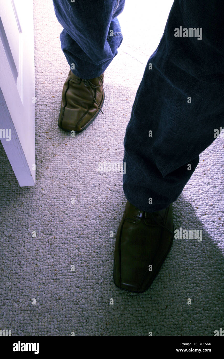 Hombre caminando en una habitación vistiendo pantalones vaqueros y zapatos marrón Foto de stock