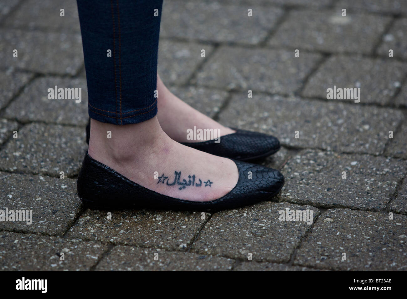 Los pies femeninos tatuados con el alfabeto árabe, zapatos negros. Foto de stock