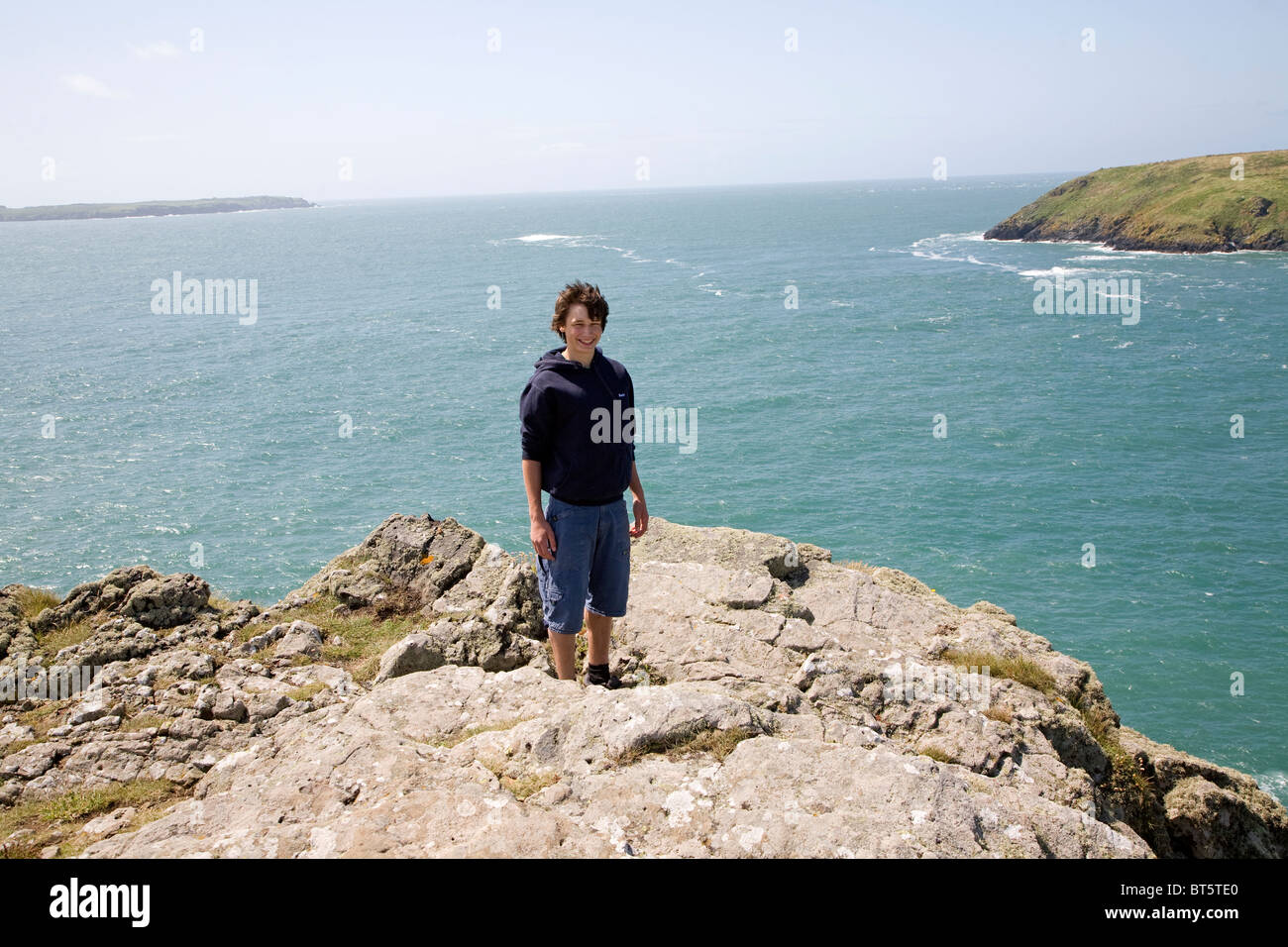 Adolescente está en fuerte viento sobre el promontorio rocoso sobre el mar Foto de stock