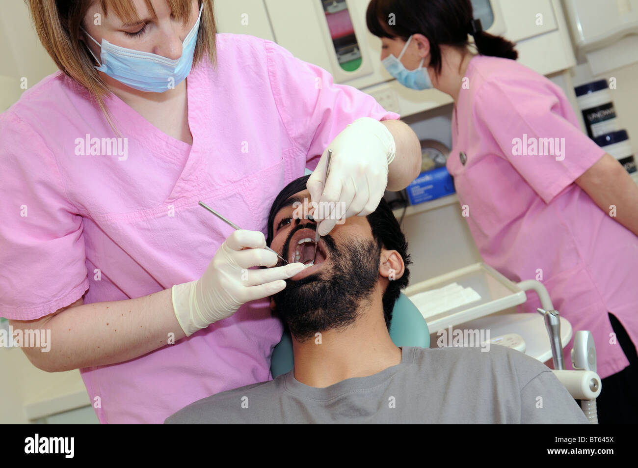 Una mujer dentista realizando un control dental en un paciente masculino con una enfermera dental en el fondo Foto de stock