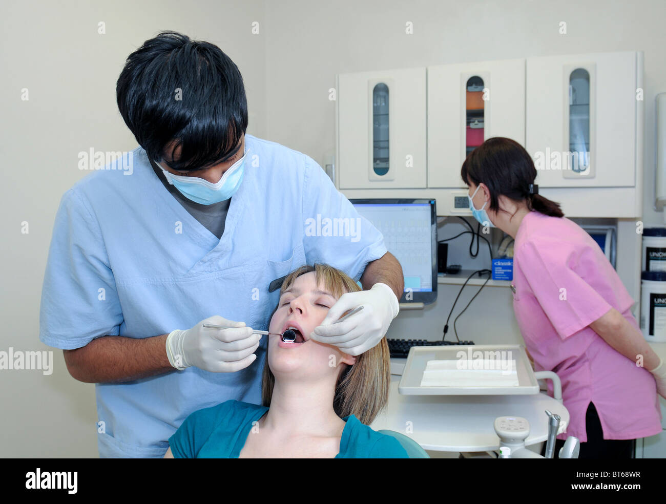 Un macho dentista realizando un control dental en un paciente con una enfermera dental en el fondo Foto de stock