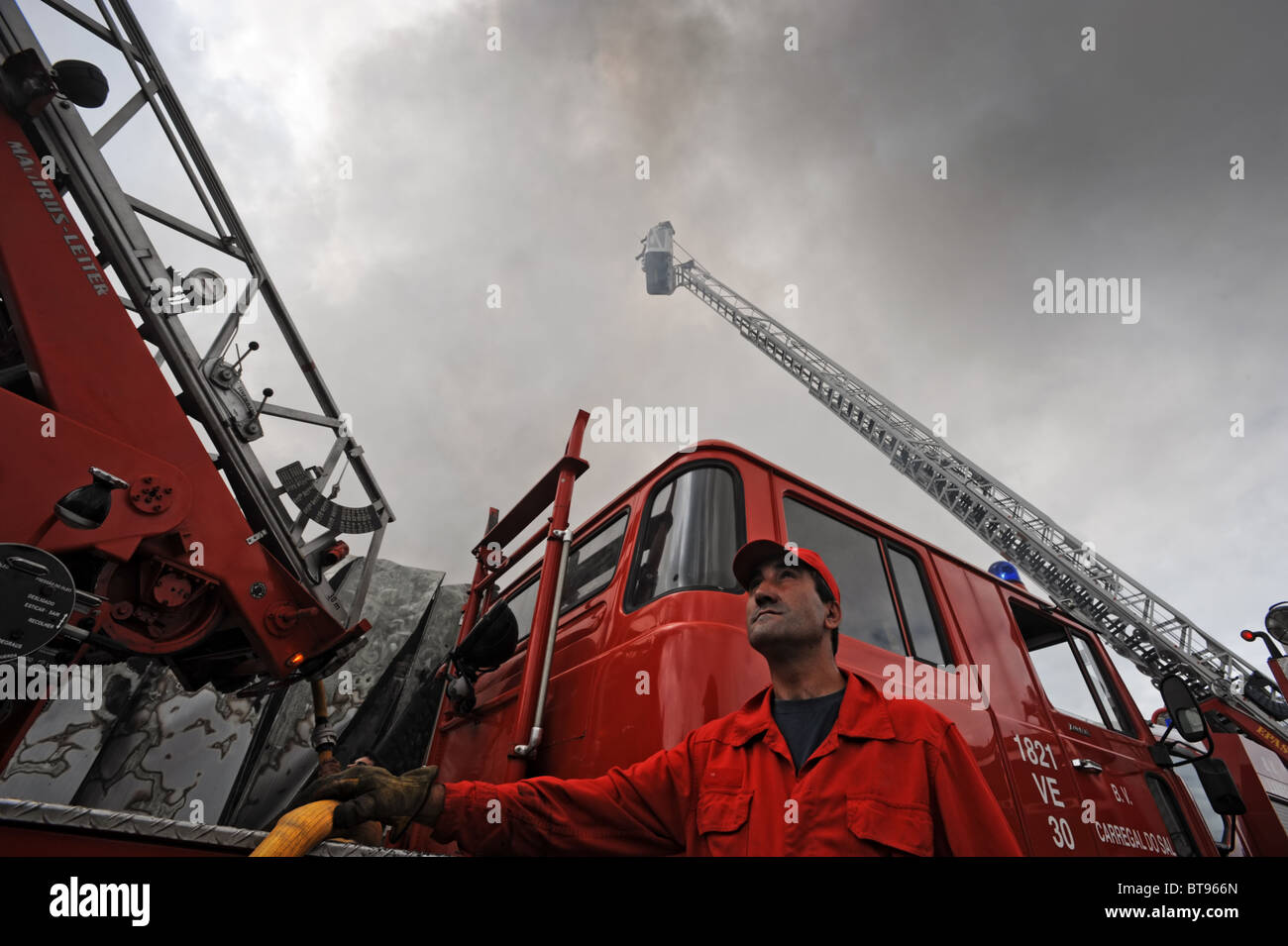 Fireman mirando hacia arriba al lado de un camión de bomberos con una escalera de extensión Foto de stock