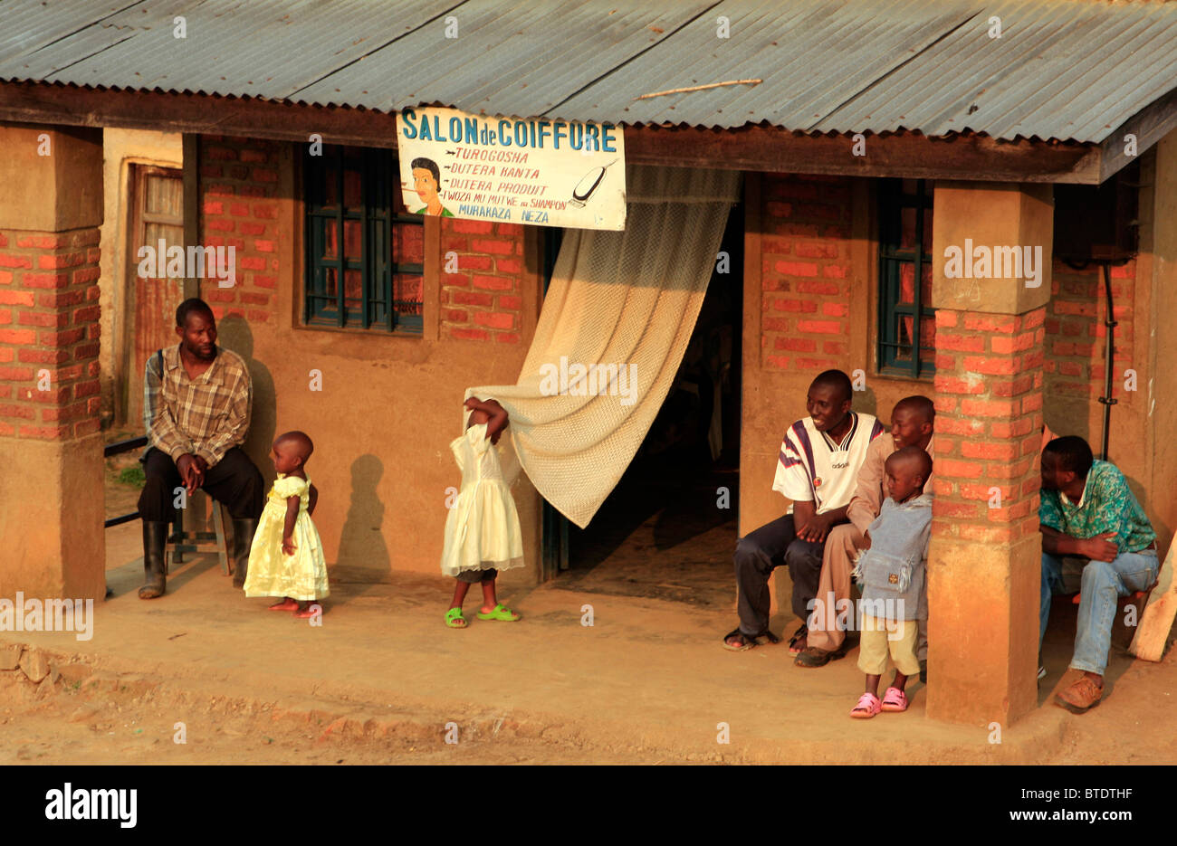 La población local, incluyendo dos niñas pequeñas en bonitos vestidos fuera una peluquería en aldea Gisankura Foto de stock