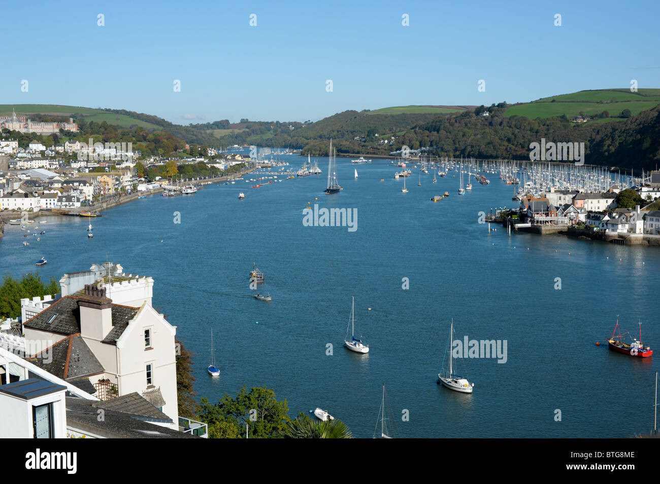 Vista desde arriba mirando el río Dart salpicado de barcos de vela con cielo despejado y el Royal Naval College en vista Foto de stock