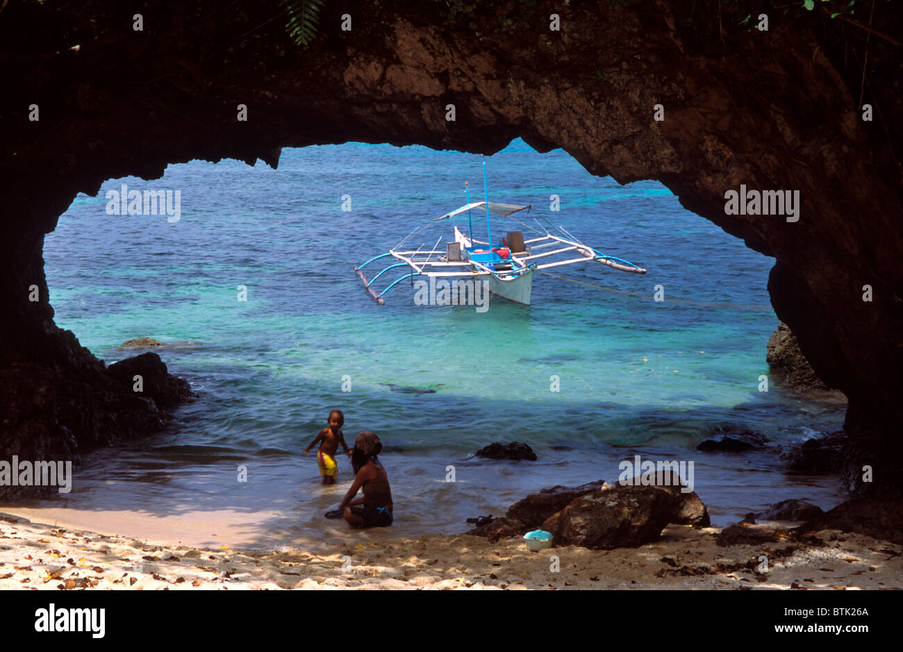 Una madre y su hijo en una cueva en la costa, donde una pequeña playa formularios en una aislada isla de Palawan en Filipinas. Foto de stock