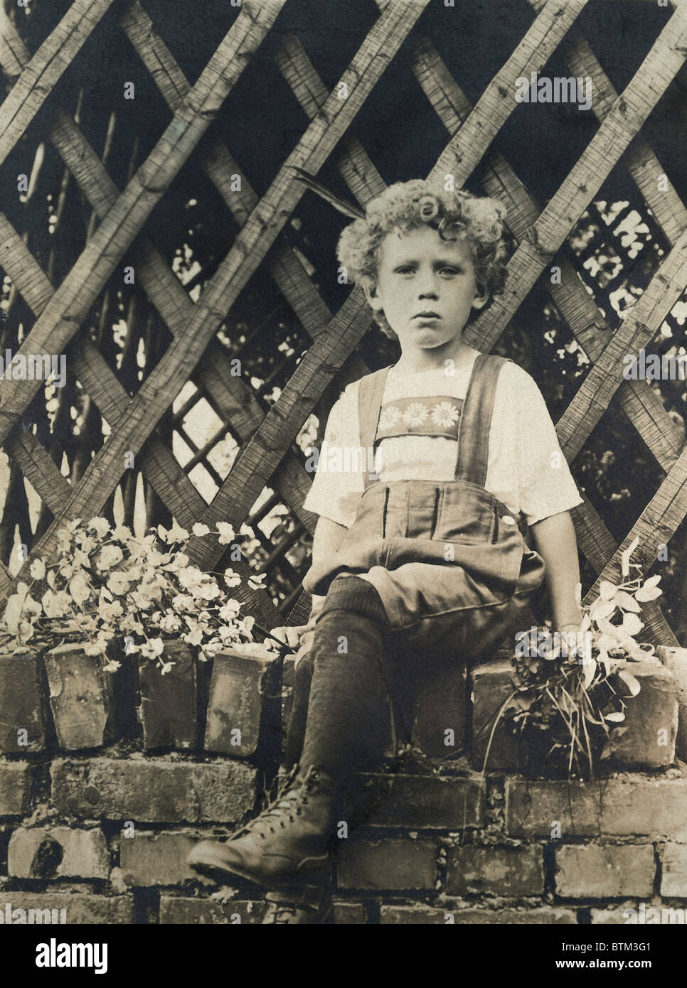 Foto histórica (1910) de un muchacho sentado en una pared. Foto de stock