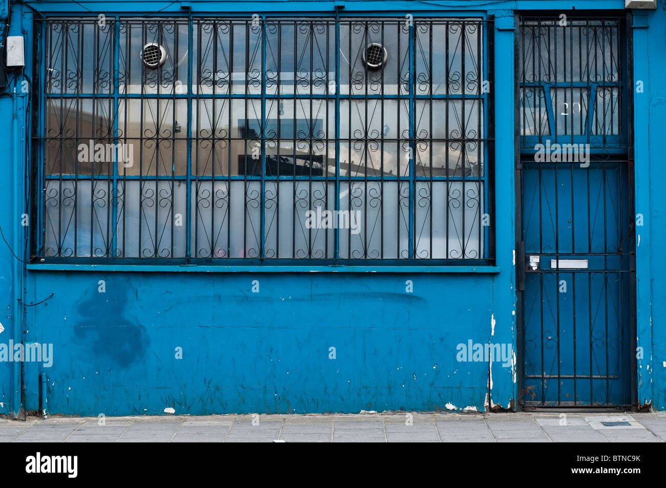 Un edificio azul en Dalson con barras en la puerta y las ventanas para la seguridad en la planta baja. Foto de stock