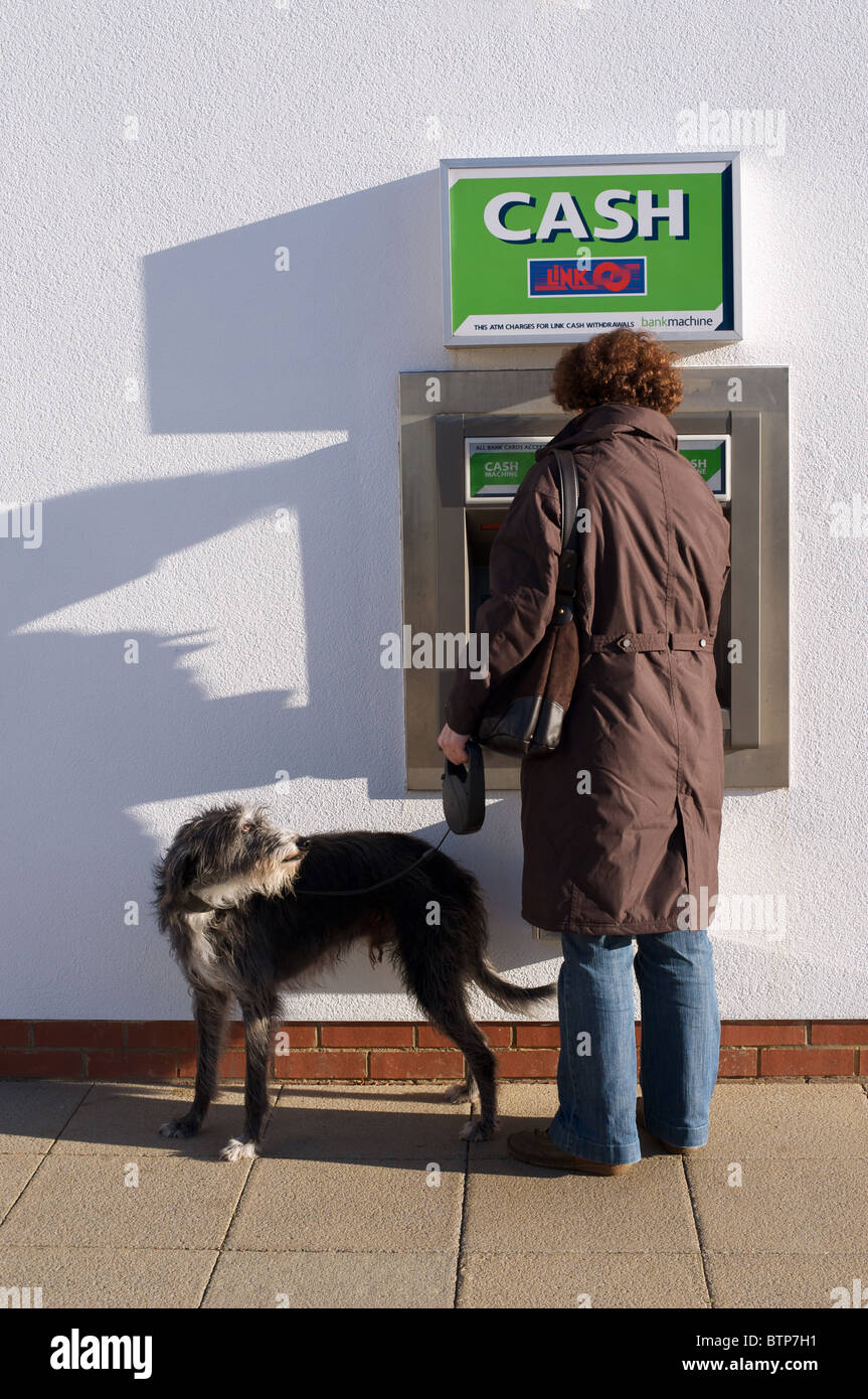 Mujer con perro mascota haciendo retiro de efectivo en cajeros Foto de stock