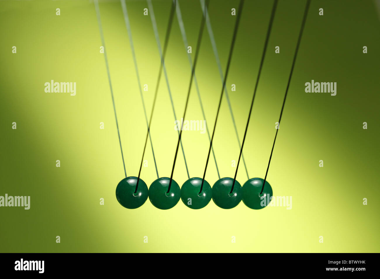 Cinco verdes canicas en fila colgando de la cadena. Ilustra Newton's cradle, un dispositivo que demuestra la conservación del impulso. Foto de stock