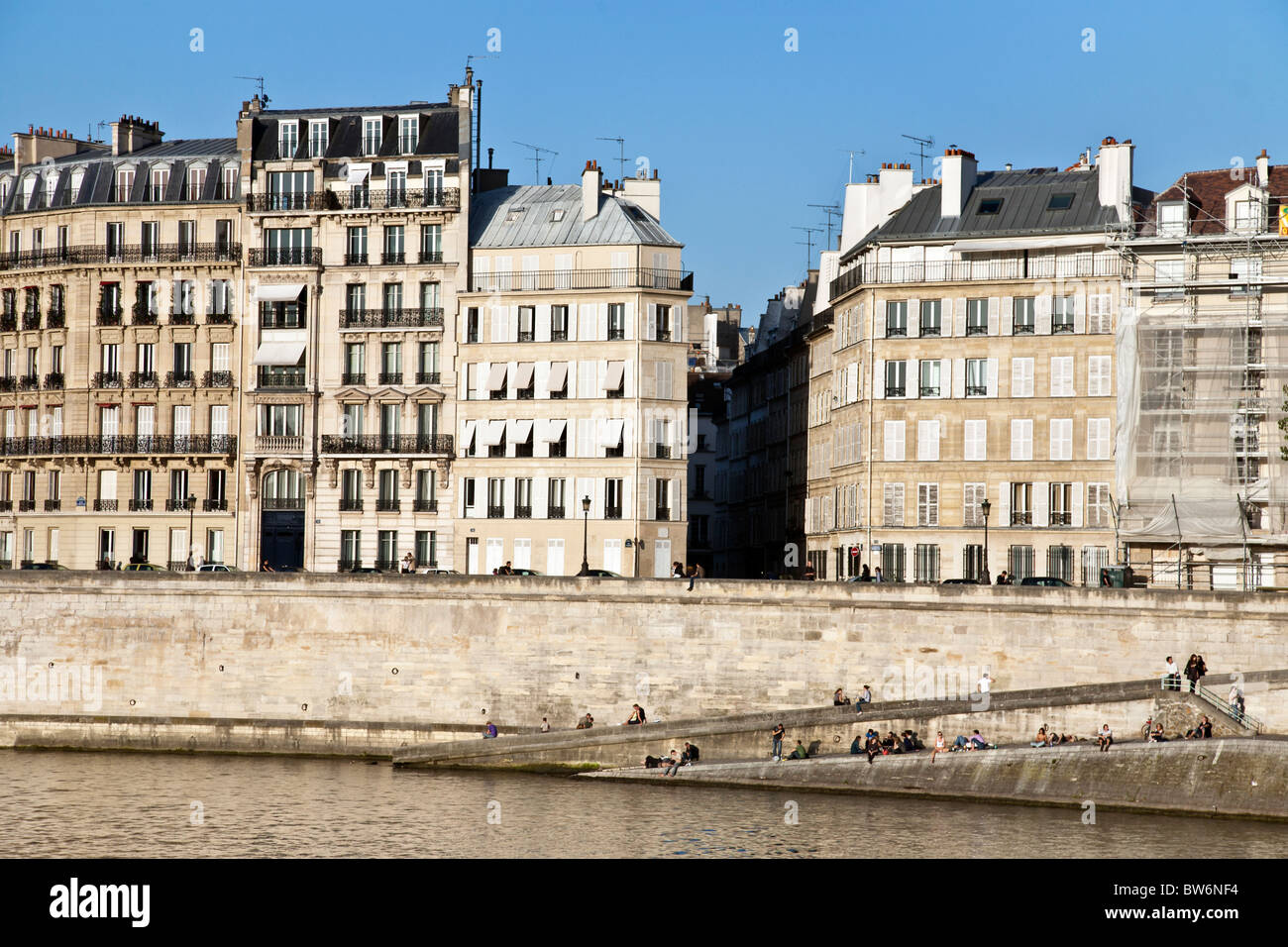 Vista a través de Sena a edificios del siglo XIX y la gente tomando sol en el histórico Quai d'Orleans de Ile Saint Louis Paris Foto de stock