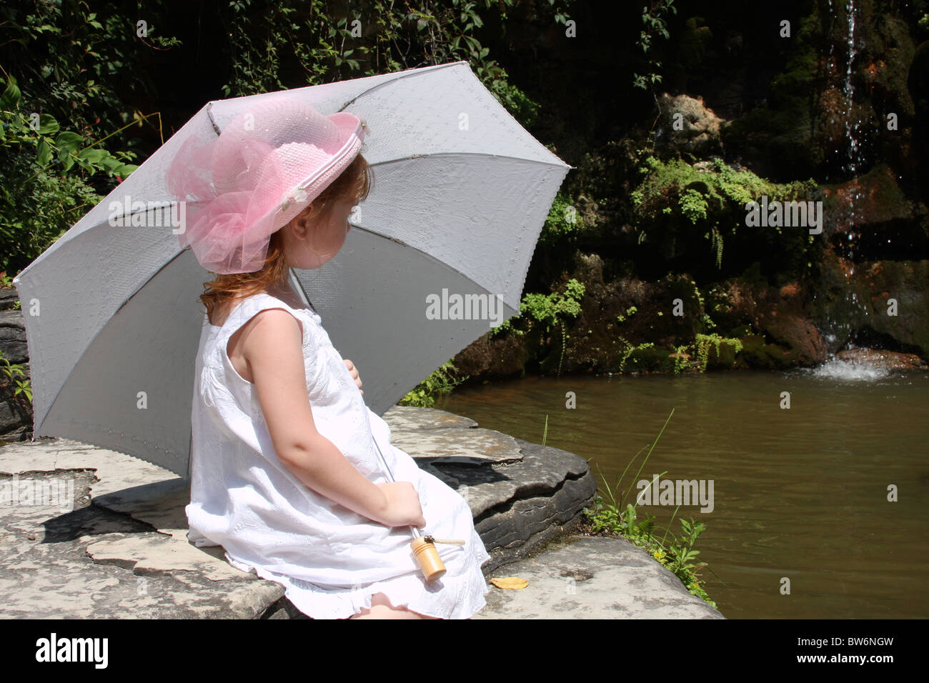 Una joven con un paraguas blanco junto a una cascada de jardín Foto de stock
