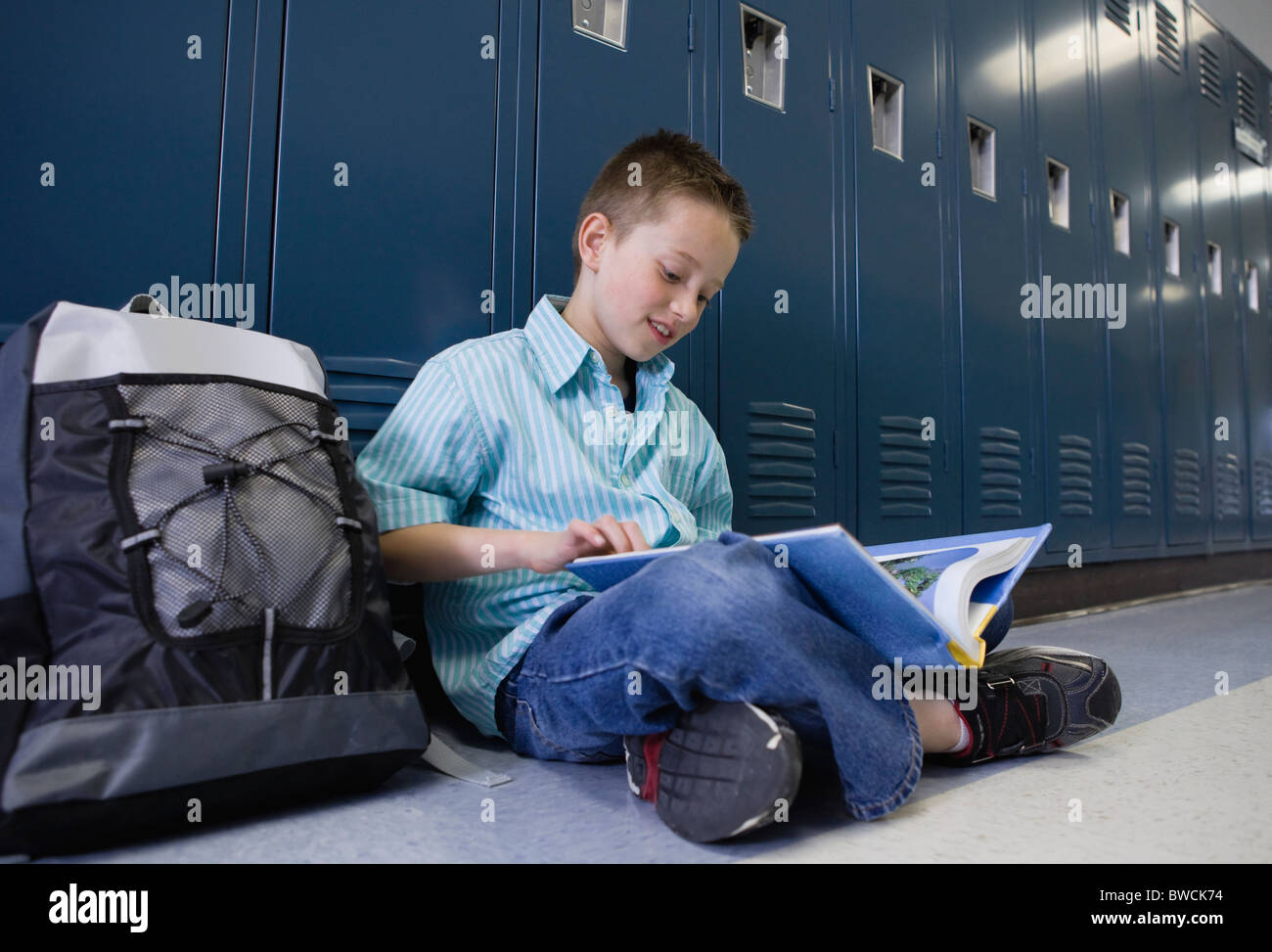Estados Unidos, Illinois, Metamora, Boy (8-9) sentados en las taquillas en la escuela corredor y libro de lectura Foto de stock